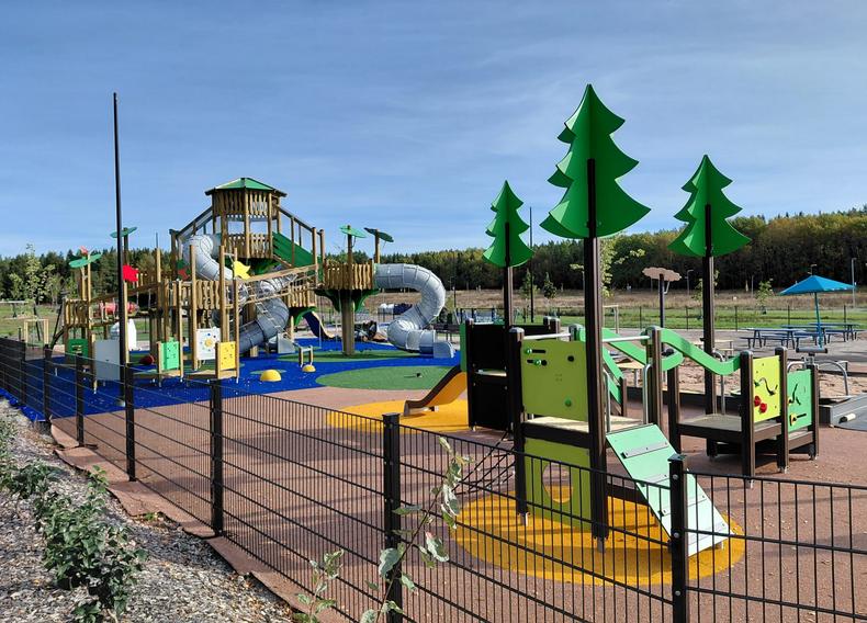 Leikkipaikalla on iso kiipeilyteline ja muita pienempiä leikkivälineitä aidatulla alueella.