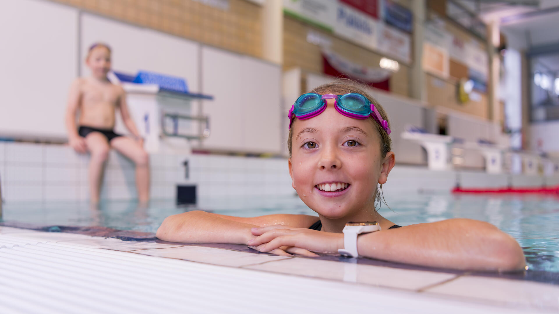 Etualalla lapsi nojaa altaan reunaan, taaempana toinen lapsi istuu altaan reunalla.