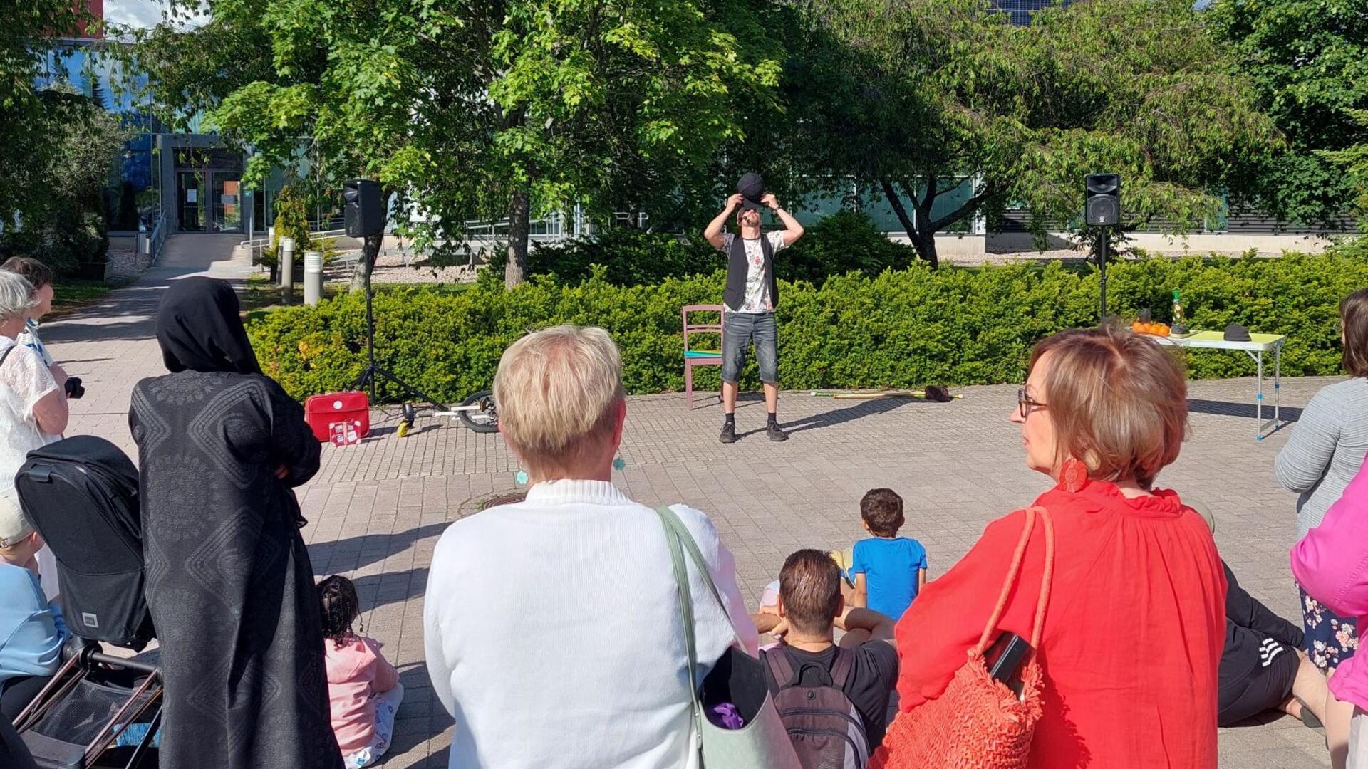 Yleisöä katsomassa sirkustaiteilijan esitystä kirjaston pihalla.