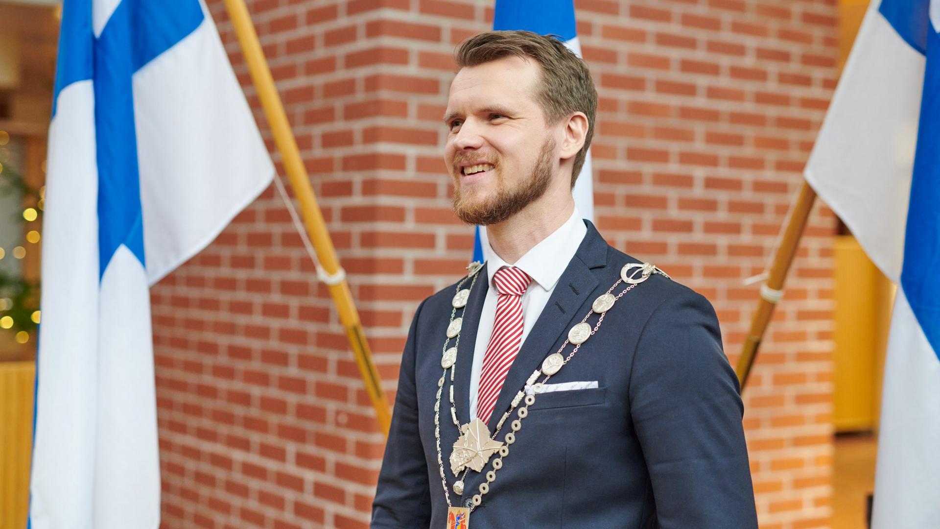 Eero Vainio Suomen lippujen edustalla käädyt kaulassa.