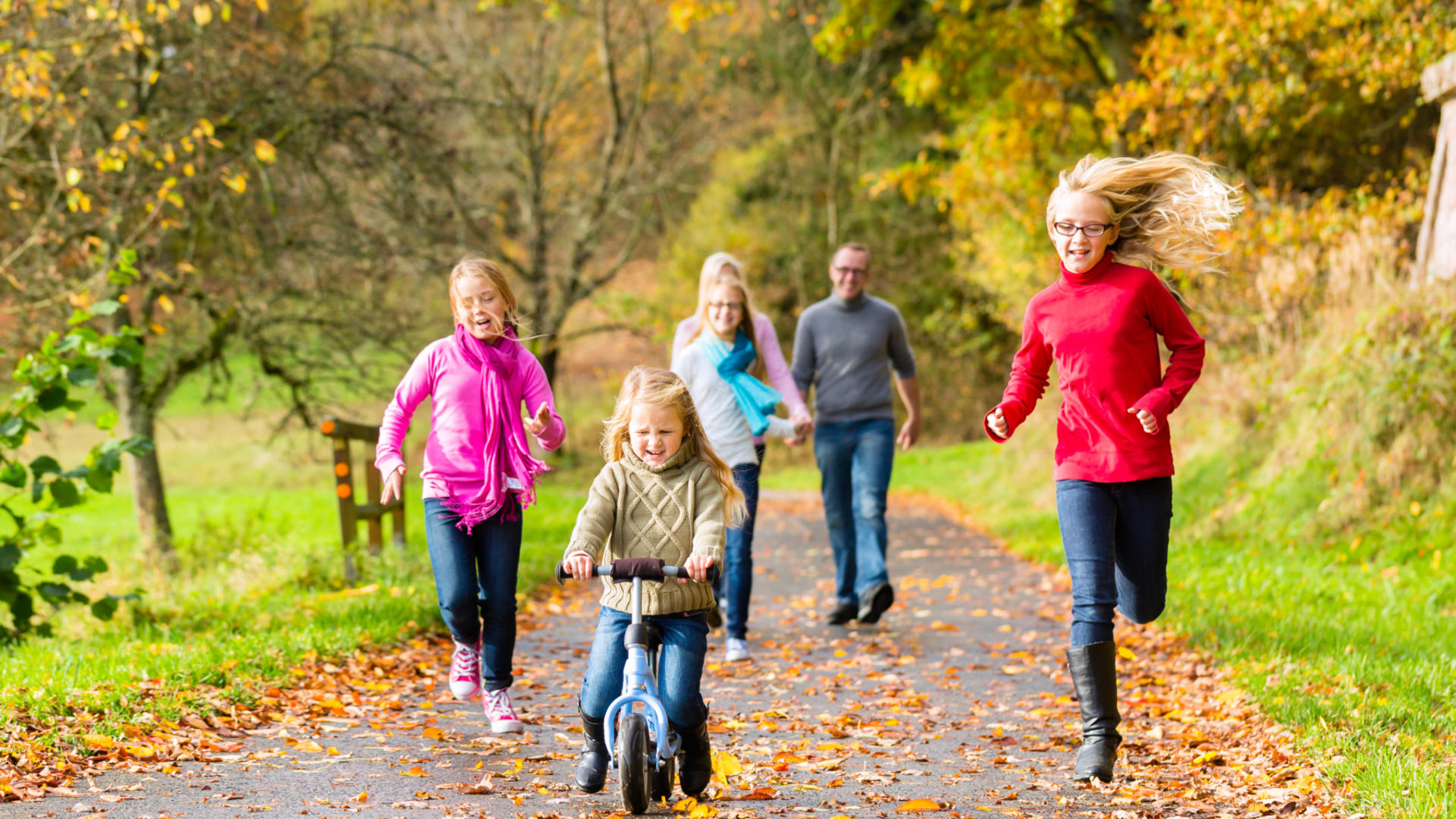 Isä, äiti ja neljä eri-ikäistä tyttöä ulkoilevat syksyisessä puistossa.