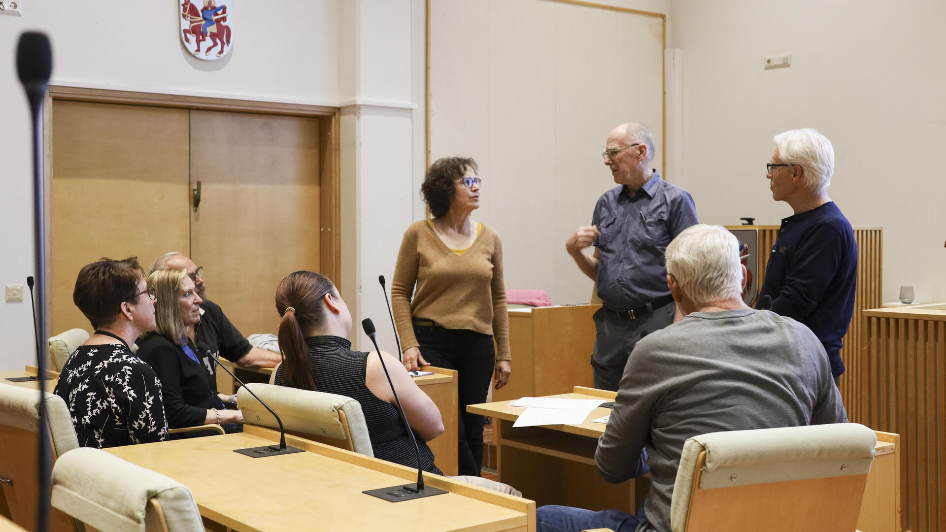 Joukko ikäihmisiä keskustelemassa valtuustosalissa.