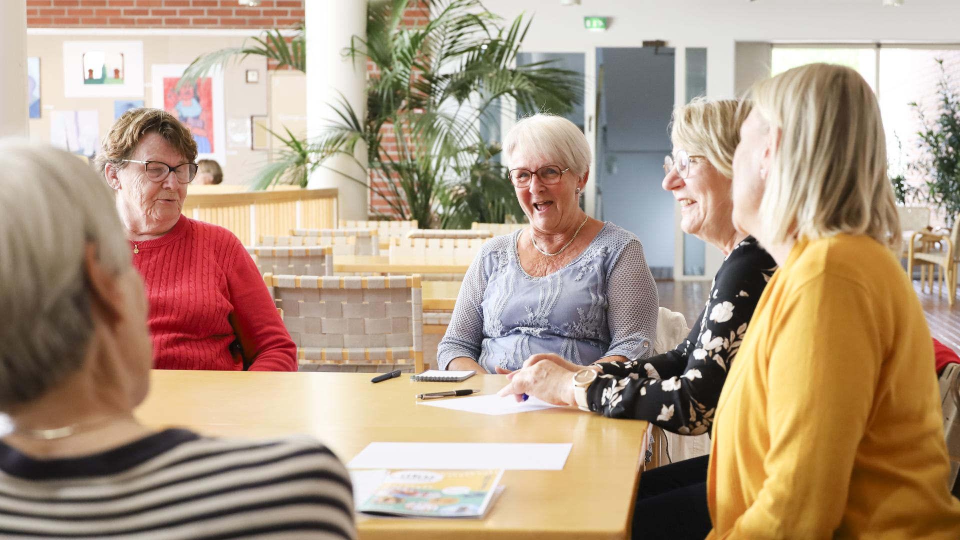 Joukko ikäihmisiä istumassa hymyillen pöydän ääressä.