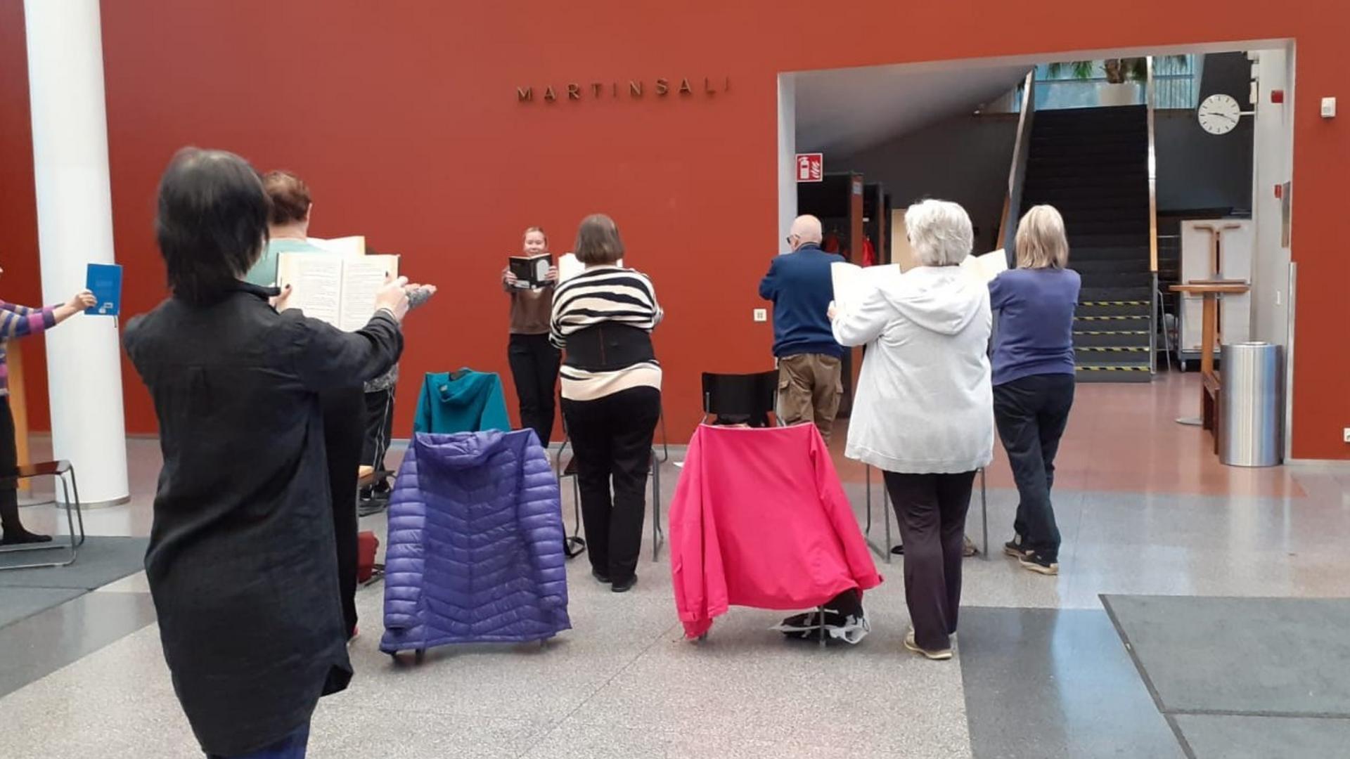 Joukko ihmisiä tasapainoilemassa kirja kädessä kirjaston aulassa.