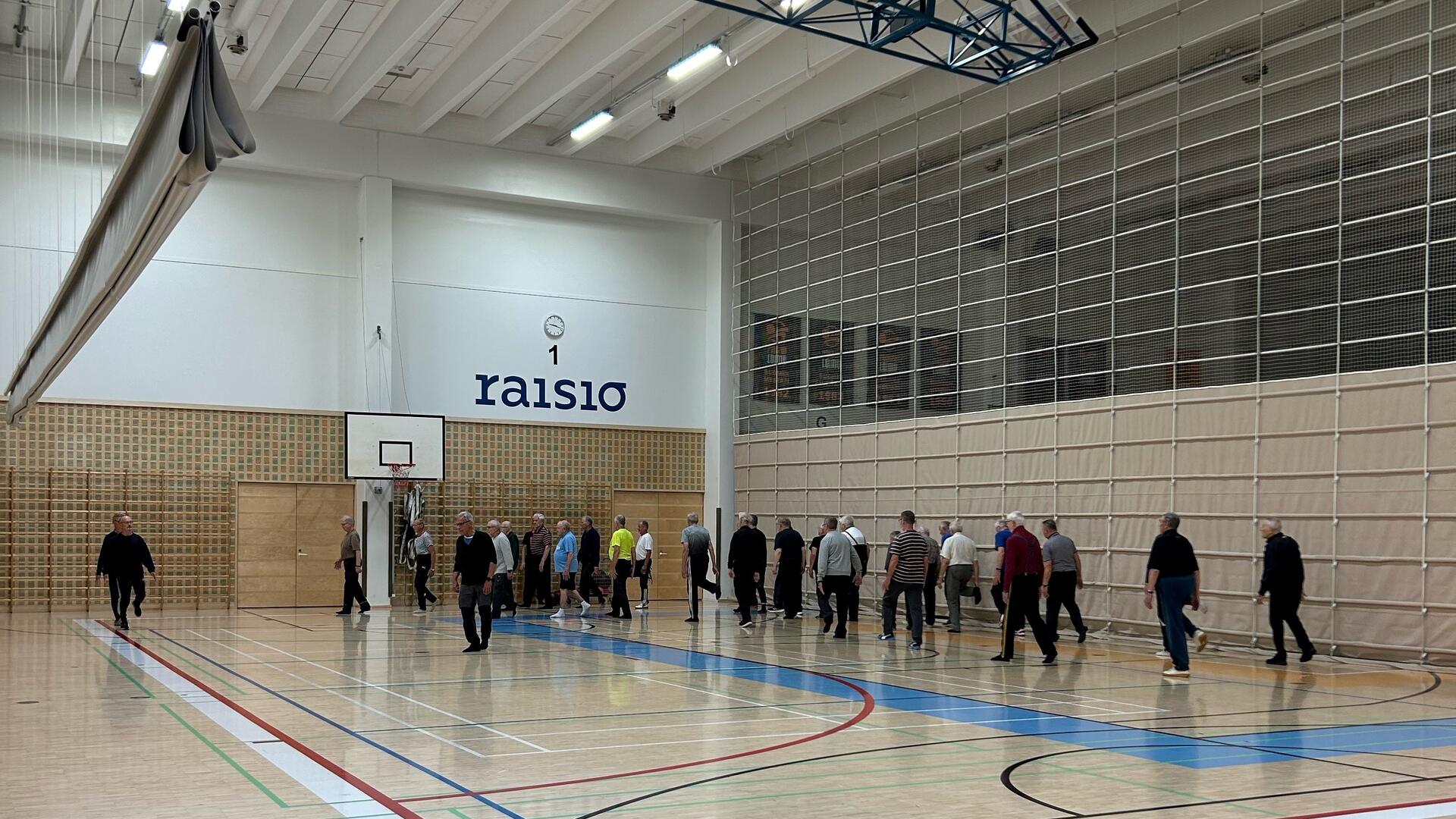 Joukko eläkeläismiehiä kävelemässä liikuntasalissa.