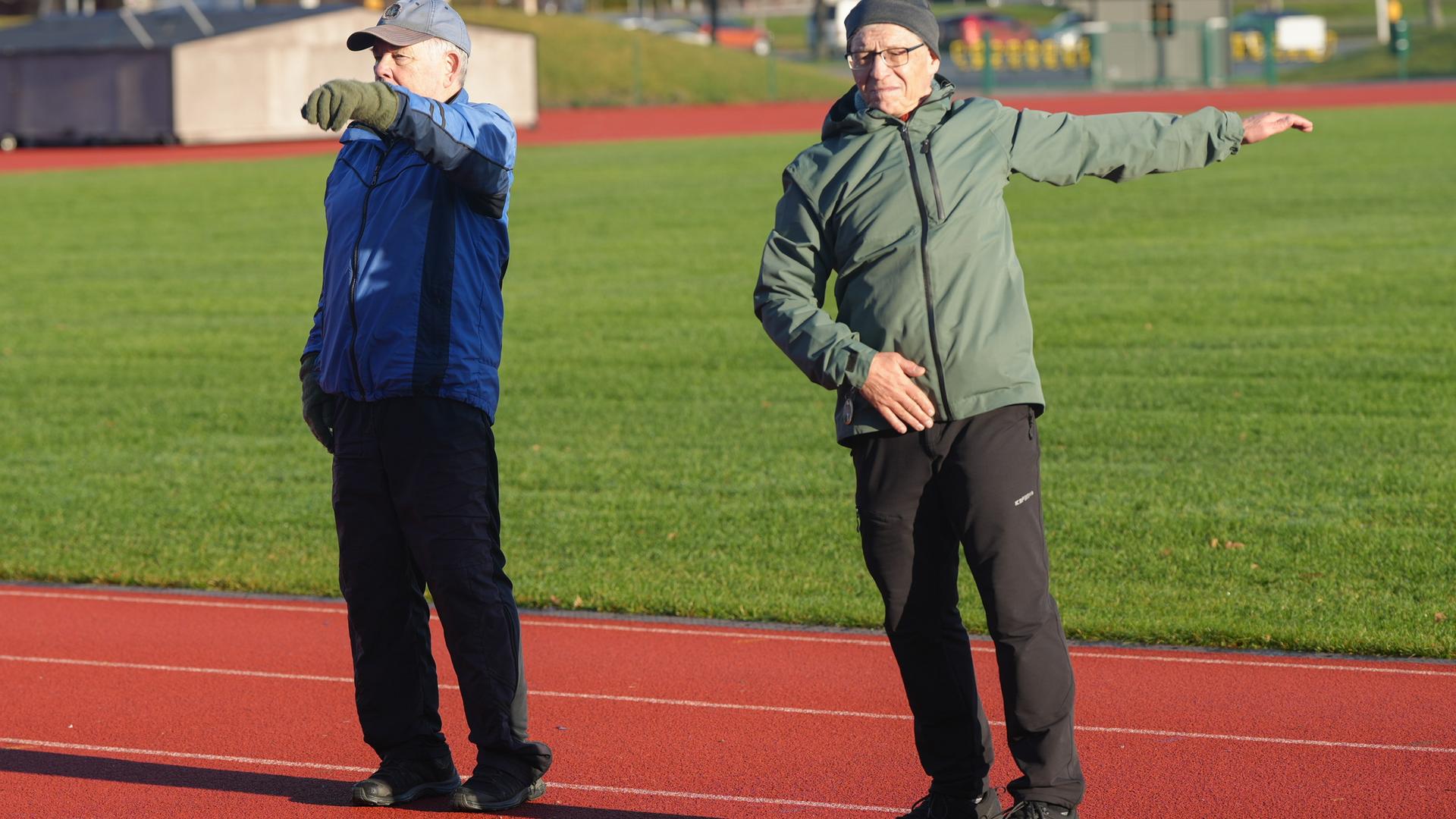 Kaksi eläkeläismiestä verryttelemässä yleisurheilukentällä.
