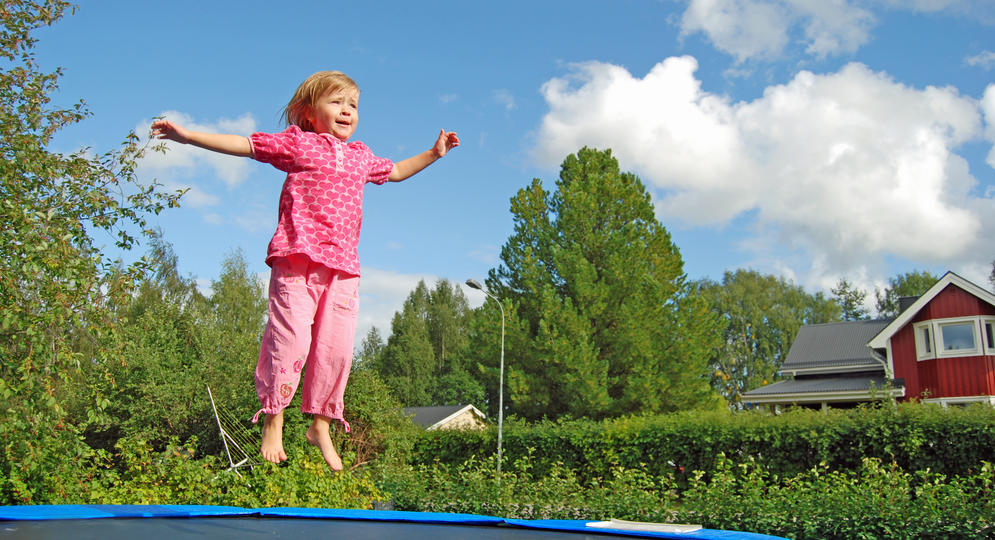 Tyttö hyppii kotipihassa trampoliinilla.