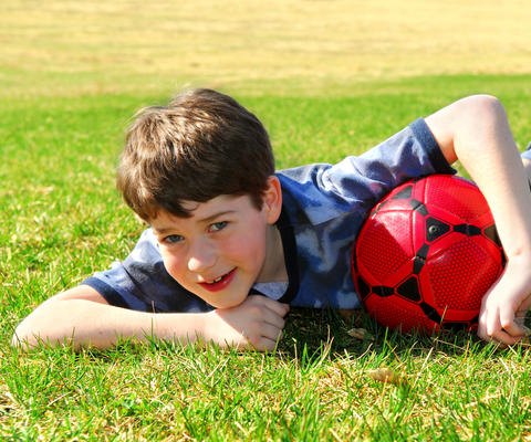 Poika makaa nurmella jalkapallo kainalossa.