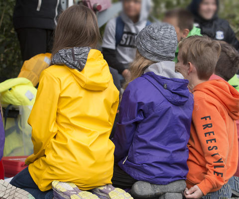 Lapset istuvat ulkona värikkäissä takeissa.