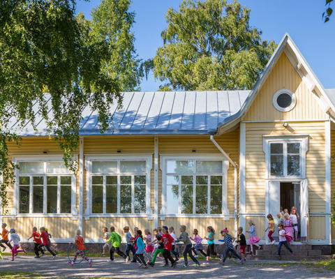 Lapsia juoksee ulos Konsan puisesta koulutalosta.