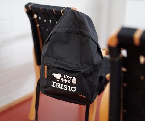 Raisio logolla varustettu reppu roikkuu tuolilla.