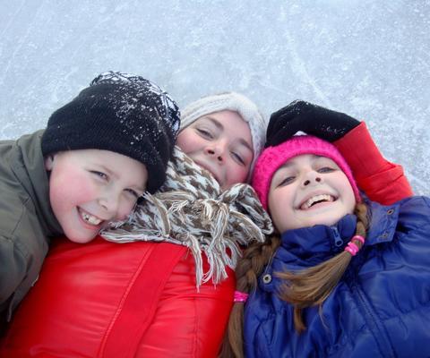 Poika ja kaksi tyttöä pötköttää nauraen jäällä.