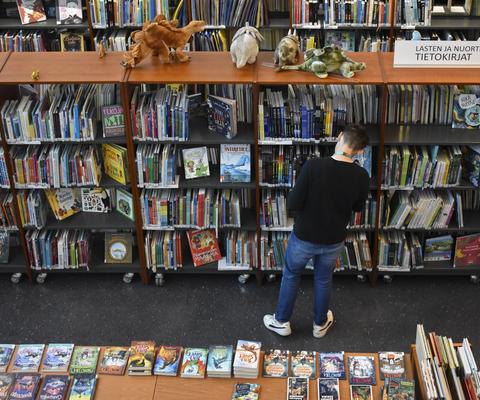 Kesätyöntekijä kirjastossa nuortenosastolla hyllyn vieressä