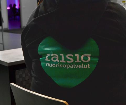 Henkilön selkä jossa hupparissa Raision nuorisopalveluiden logo
