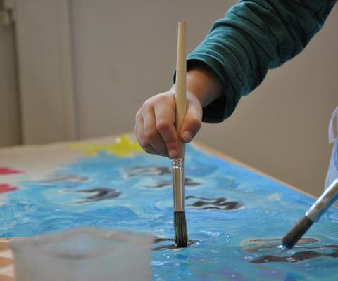 Lapsi pitää pensseliä ja maalaa sinisellä värillä.