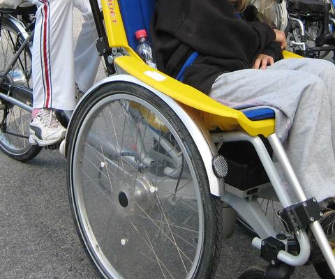 Avustaja polkee pyörää, jossa on pyörätuoli edessä.