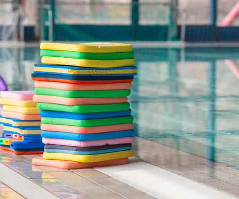 Värikkäitä uintilautoja pinossa altaan reunalla.