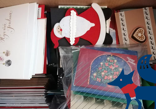 Paljon joulukortteja laatikossa. Alakulmassa sininen kettu, jolla on jouluinen, punainen kaulaliina.
