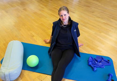 Liikuntaneuvoja istuu jumppamaton päällä ja hymyilee