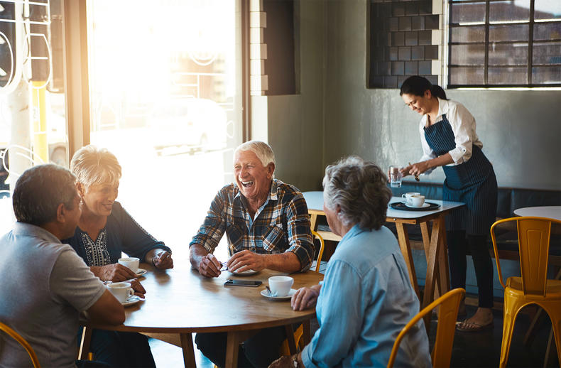 Neljä seniori-ikäistä henkilöä kahvilassa rupattelemassa. Taustalla kahvilatyöntekijä.