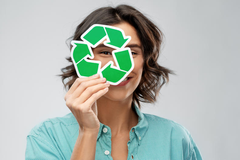 Henkilö pitää kasvojensa edessä vihreää kierrätysmerkkiä.