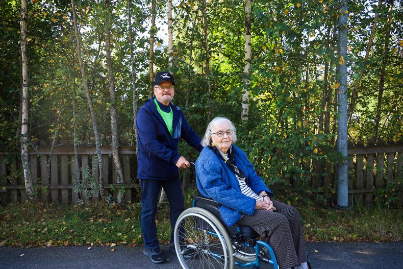 Ilkka ja Leena poseeraavat kameralle. Leena istuu pyörätuolissa ja Ilkka seisoo pyörätuolin takana.