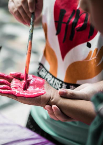 Kaksi henkilöä maalaa toistensa käsiä pinkillä sormivärillä. 