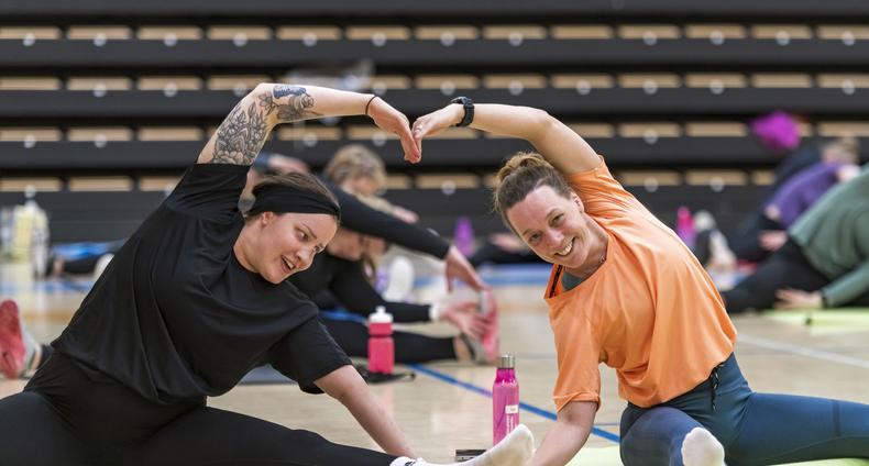kaksi naista jumppaa ja muodostavat sydämen käsillään.