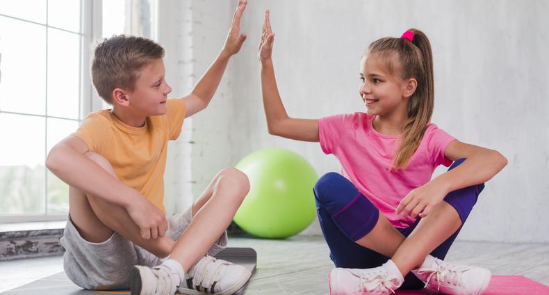 Lapset istuvat jumppamatoilla ja lyövät kädet yhteen.