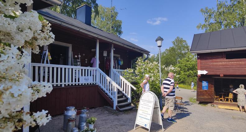 Krookilan kotiseutukeskuksen pihapiiri, jossa punaiset puurakennukset. Rakennuksen edessä kyltti ja kaksi ihmistä sekä kukkiva puu tai pensas.