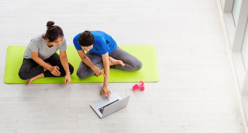 Kaksi naista istuu jumppamatolla ja tutkivat tietokonetta.