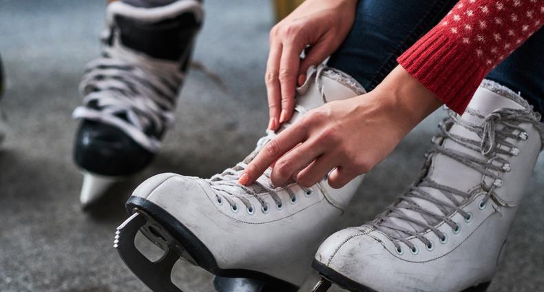 Nainen sitoo taitoluistimien nauhoja, taustalla hokkarit.